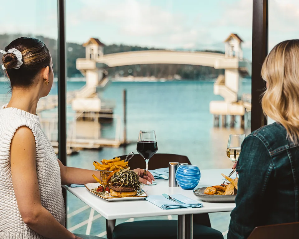 Guests dining at Dockside beside windows overlooking the lake and marina bridge.